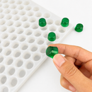 Hand holding an emerald green gumdrop beside a 3mL gumdrop gummy mold with 262 cavities on a white background